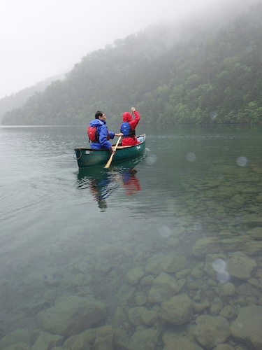 小雨混じりの然別湖でカヌーを漕いでいる様子を写したツアー写真